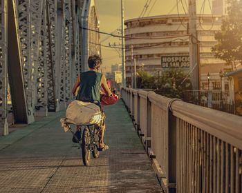 Rear view of man riding bicycle on bridge in city