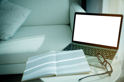 High angle view of book and eyeglasses with laptop on table at home