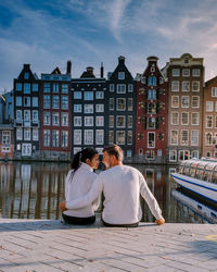 Rear view of couple sitting on building against sky