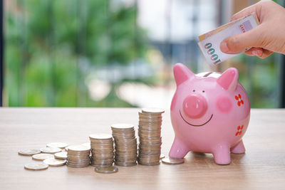 Midsection of woman putting coin in piggy bank at table