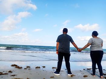 Rear view of men standing on beach against sky