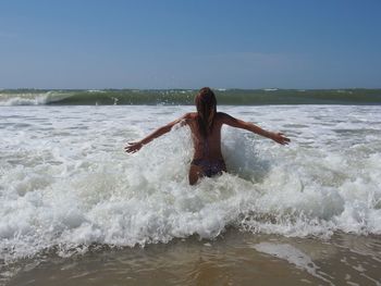 Rear view of woman with arms outstretched standing in sea against sky