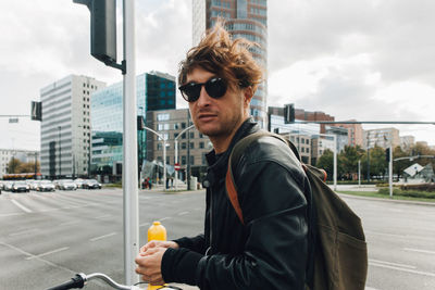 Young man wearing sunglasses on street in city against sky