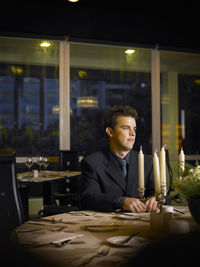 Young man sitting at table in illuminated restaurant