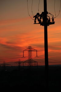 Low angle view of silhouette electricity pylon against orange sky