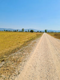 Dirt road amidst field against sky