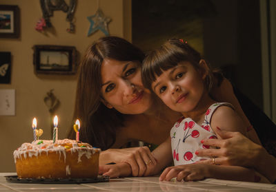 Portrait of mother and daughter with birthday cake at home