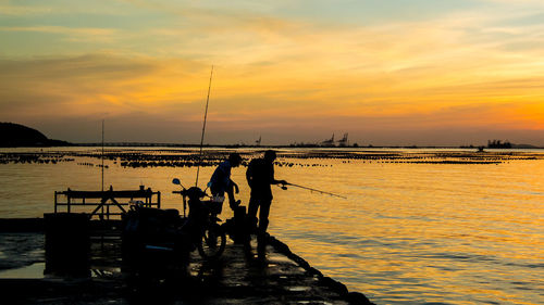 Silhouette men fishing in sea at sunset