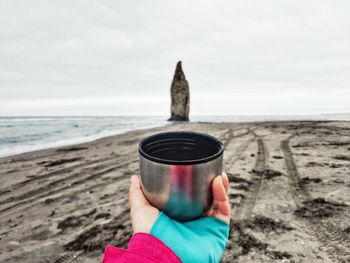 Close-up of hand holding sunglasses on beach against sky