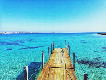 Pier over sea against clear blue sky
