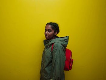 Smiling young woman standing against yellow background