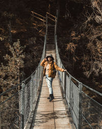 Front view of young woman standing on hanging footbridge in autumn
