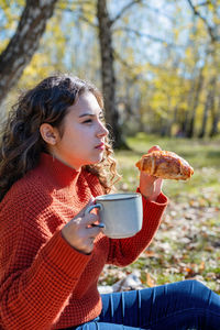 Leisure, free time. beautiful caucasian woman in red sweater on a picnic outdoors, sitting on a pla