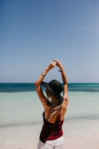 Woman in hat standing at beach against clear sky in sunny day