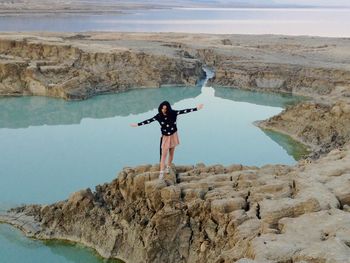 Young woman with arms outstretched standing on cliff by lake