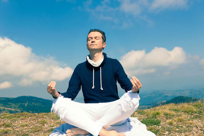 Young man sitting on land against sky