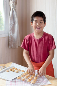 Portrait of cheerful boy placing food on cooling rack at table