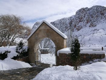 Snow covered house by building against sky