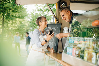 Female owner showing smart phone to male coworker while standing by food truck