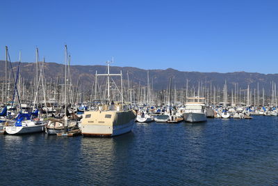 Boats moored at harbor against clear blue sky