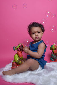 Baby girl playing with toys while sitting on fur rug against pink wall