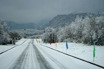 Snow covered road by mountain against sky