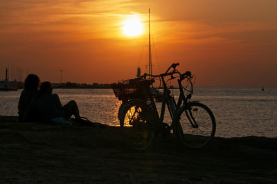 Bicycles on beach against sky during sunset