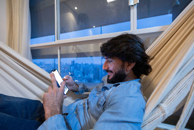 Young man with smartphone at night on a hammock city view background. mobile, technology