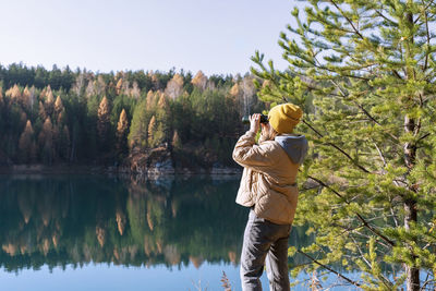 Young woman looking through binoculars at birds on lake against autumn forest birdwatching, ecology