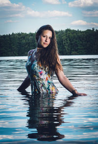 Portrait of young woman in lake against sky
