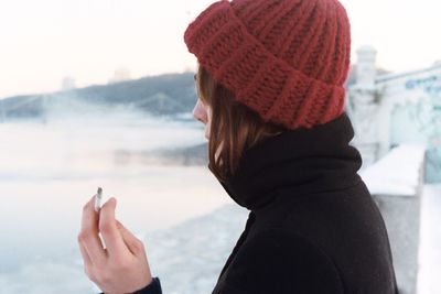 Young woman with cigarette standing at lake against sky