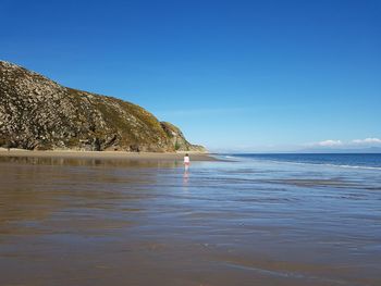 Rear view of woman on shore at beach against blue sky