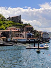 Sailboats in river by buildings against sky