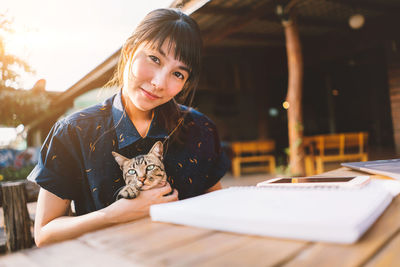 Portrait of young woman with cat sitting on table