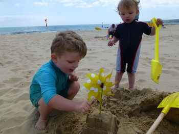 Brothers making sandcastle at beach against sky