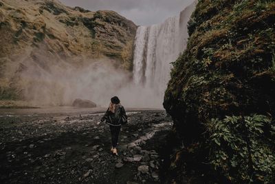 Rear view of woman walking on rock against waterfall