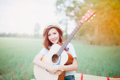 Young woman with guitar on grassy field at park