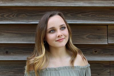 Smiling teenage girl looking away against wooden wall