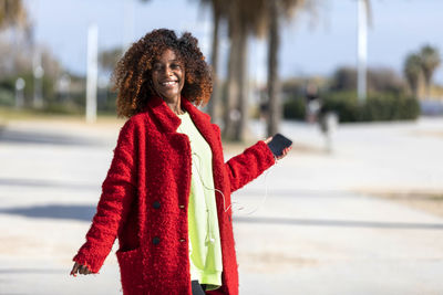 Portrait of woman dancing while listening music on mobile phone against trees