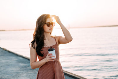 Young woman wearing sunglasses standing against sea