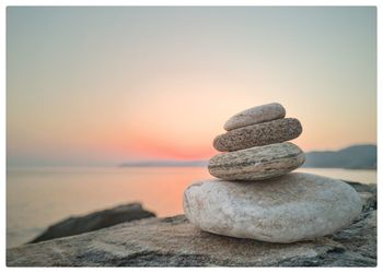 Stack of stones on beach against sky during sunset