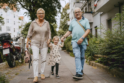 Happy grandparents holding hands of granddaughter while walking at street