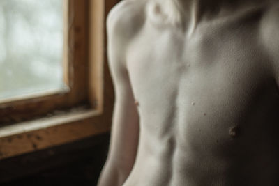 Close-up of shirtless man standing by window