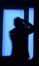 Rear view of silhouette woman standing against blue background