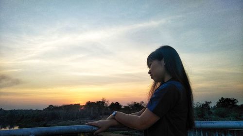 Side view of woman sitting against sky during sunset