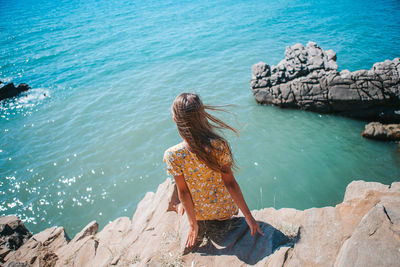 Rear view of woman sitting on rock by sea