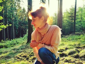 Young woman looking away while sitting on land in forest