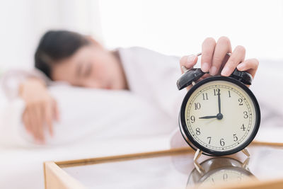 Woman sleeping with hand on alarm clock in bedroom