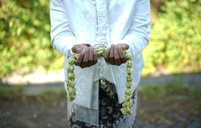 Midsection of traditional groom standing in park holding jasmine necklace