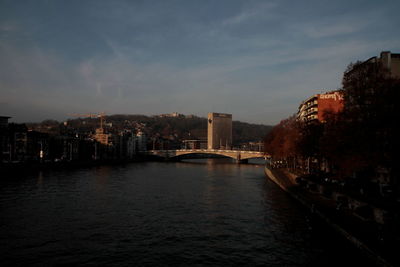 Bridge over river by buildings in city against sky